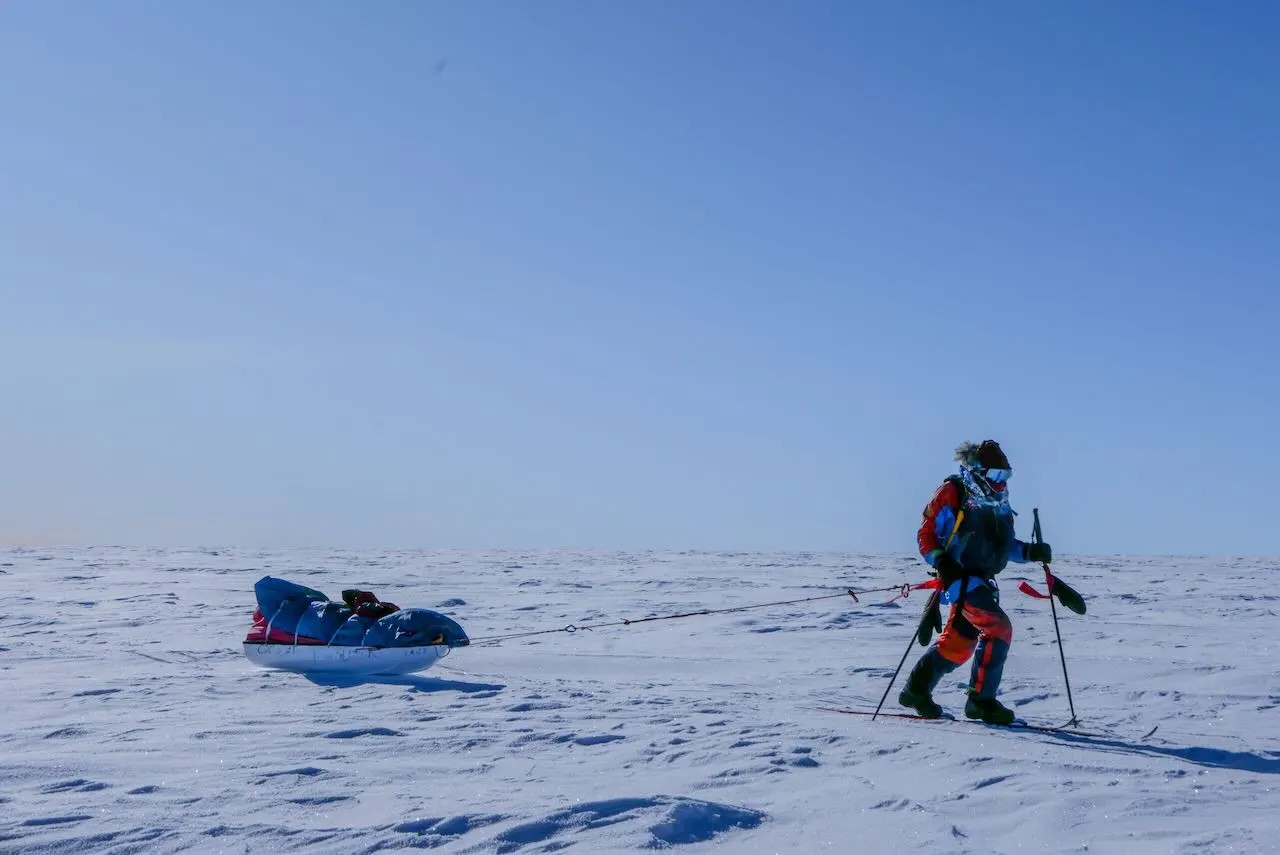 Ben Weber hauling a loaded pulk on skis across a flat polar plateau under a clear blue sky