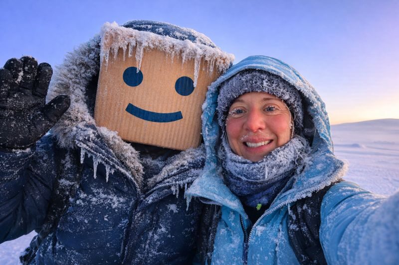 Erica Stanford with 'Boardy' — a frost-covered companion with a cardboard smiley for a head — at golden hour on the snow — training for the Polar Dogs Antarctica Expedition