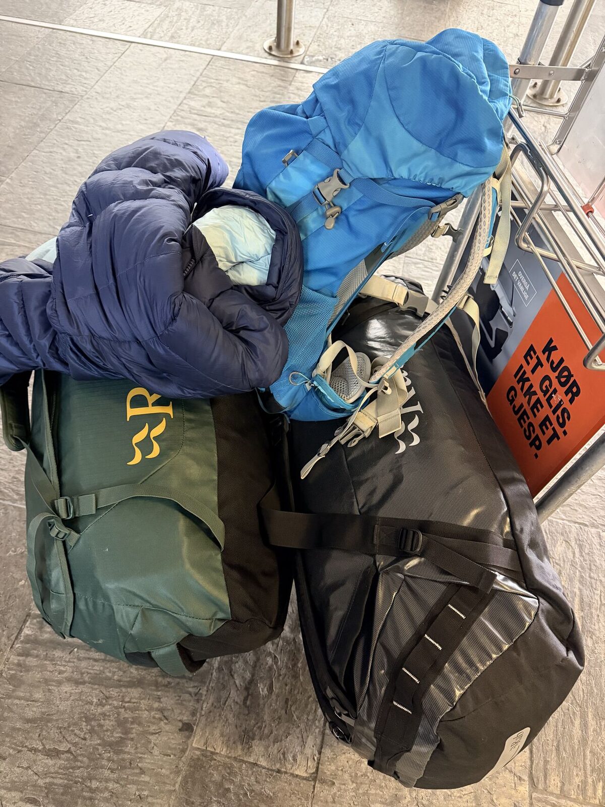 Duffels, pack and down jacket stacked on an Oslo airport trolley — two weeks of polar survival training, packed