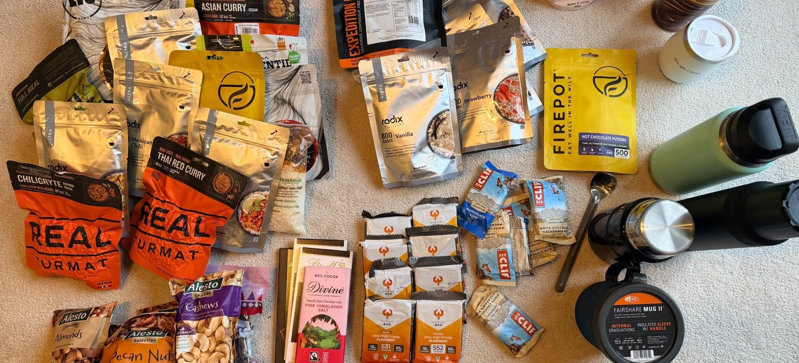 Dehydrated expedition meals, energy bars, nuts, dried fruit, chocolate, a flask and a stove laid out on the floor, one week of vegan expedition food for a polar training trip