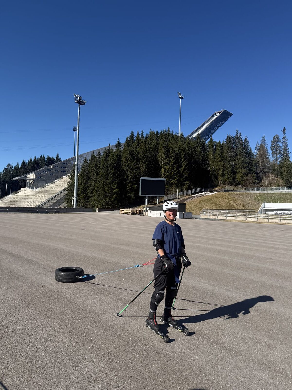 Erica Stanford roller skiing with a tyre in tow at the Holmenkollen ski arena in Oslo, the ski jump towering behind — training for the Polar Dogs Antarctica Expedition